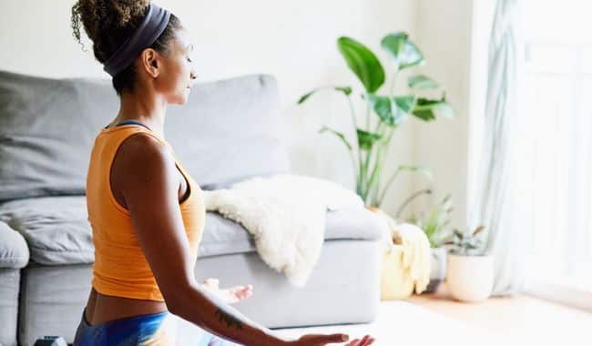 Une femme assise chez elle en méditation, suggérant que la méditation de pleine conscience peut être bénéfique pour atténuer la douleur et favoriser le bien-être.