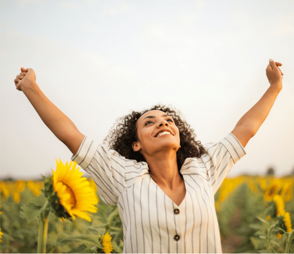 Femme jeune souriante les bras en l’air dans un champ de Tournesols qui pratique la gratitude