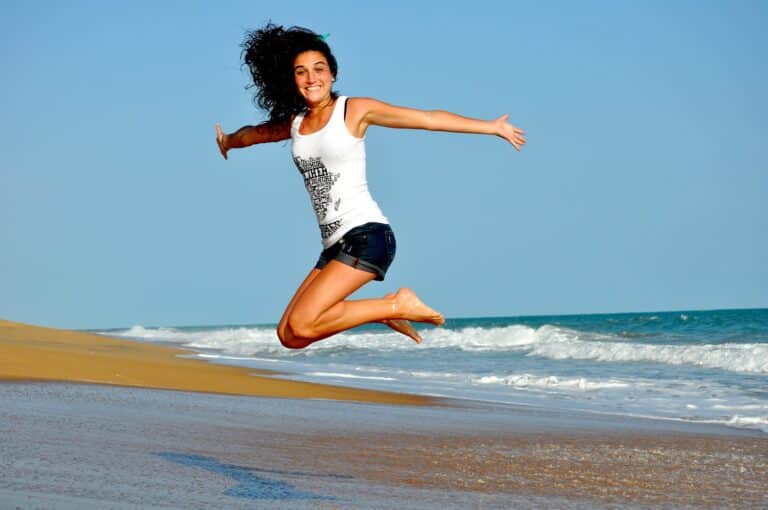 améliorer son bien-être physique grâce à la positivité femme souriante qui saute à la plage